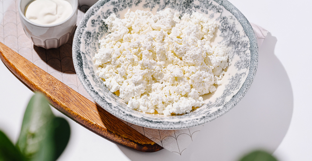 Творог в миске рядом со сметаной, пример ферментированных продуктов для поддержки микрофлоры