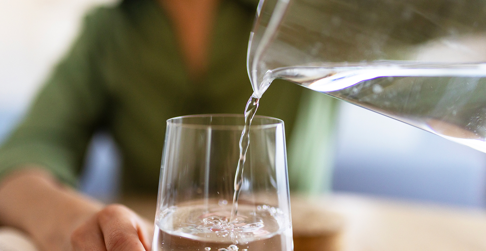 Вода наливается в стакан из кувшина — питьевой режим как основа здорового пищеварения и профилактики запоров