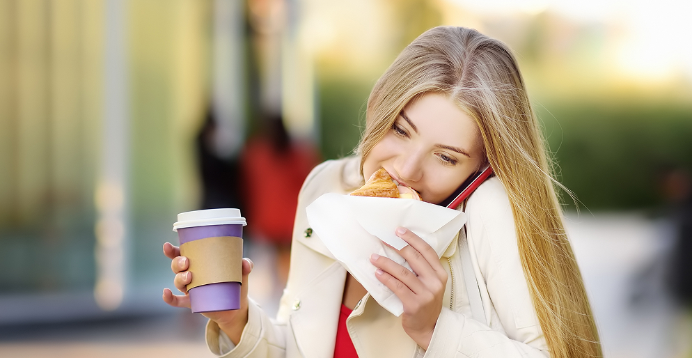 Девушка перекусывает круассаном на ходу с кофе — пример вредной привычки питания, нарушающей микрофлору кишечника