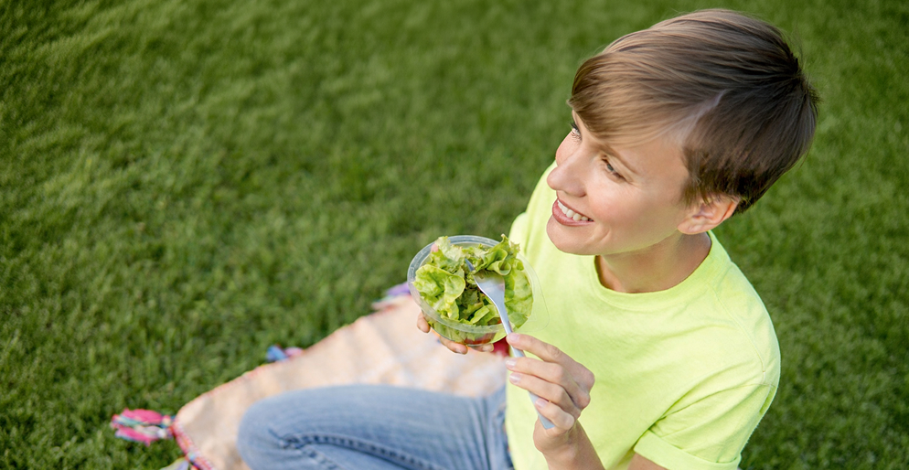 Девушка ест свежий салат из зелени на природе — клетчатка и пребиотики в рационе для здоровья кишечника